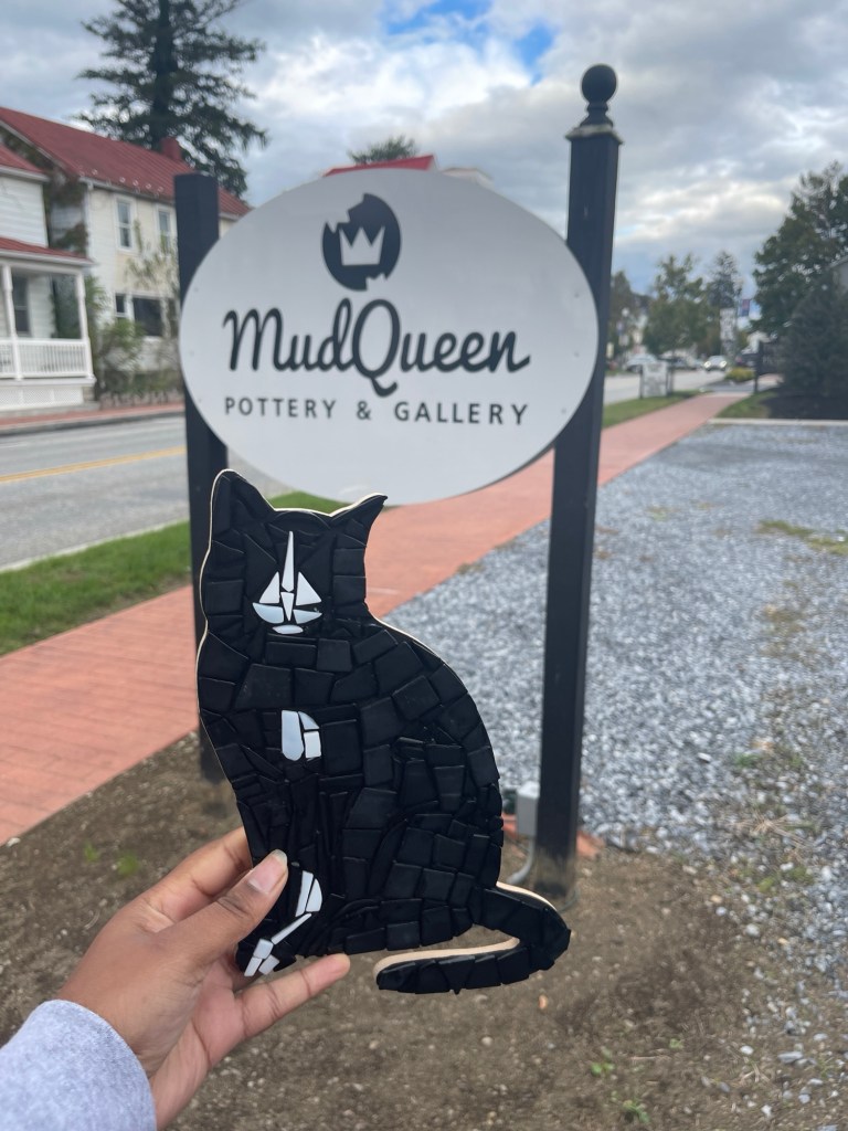 Kristian Beverly holds up ceramic cat next to mud queen sign